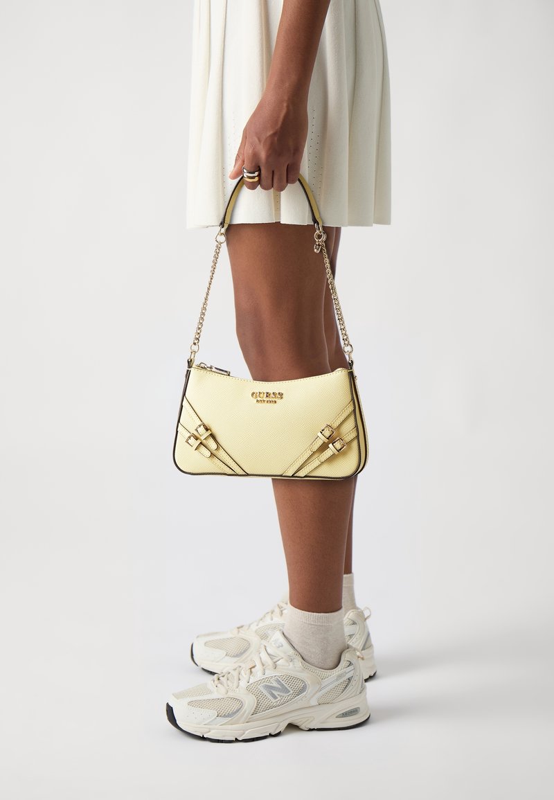 Yellow handbag with textured finish, featuring a black trim and gold hardware. It has a chain strap and decorative straps across the front.