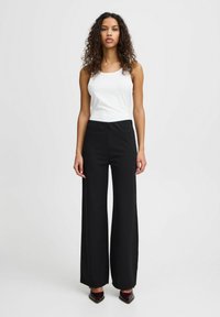 Černé široké kalhoty s elastickým pasem, které jsou doplněny o upnutý bílý top bez rukávů. Hladká textura a minimalistický design.
