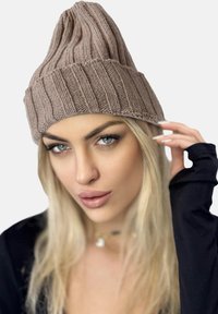 Gorro de punto en marrón claro con canalé vertical, punta afilada y un dobladillo. El material parece suave y texturizado.