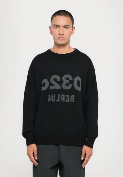 Schwarzer Strickpullover mit großen grauen Buchstaben "0320 BERLIN". Er hat einen weiten Rundhalsausschnitt und lockere Ärmel.