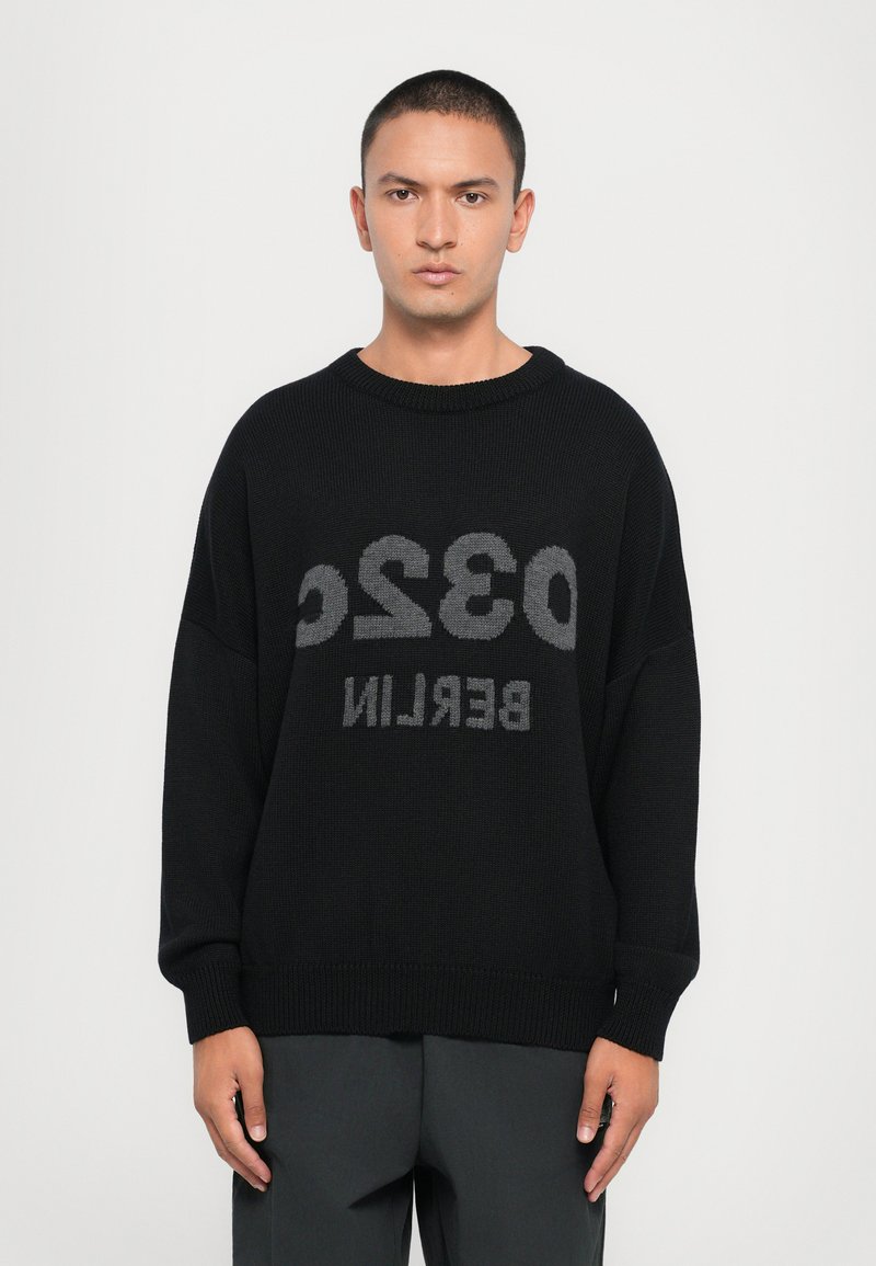Pull en tricot noir avec un grand texte gris indiquant "0320 BERLIN." Il a un col rond large et des manches lâches.