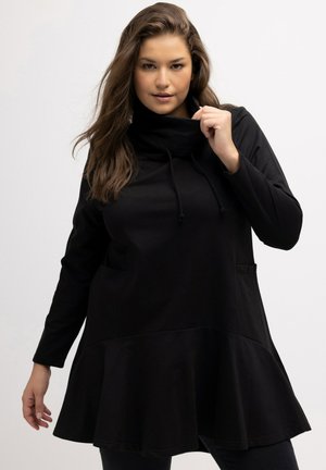 Tunica nera con scollo a cerniera, maniche lunghe, orlo svasato e tasche frontali; realizzata in morbido cotone testurizzato.