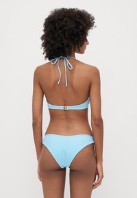 Svijetloplavi bikini s dizajnom halter vrata, podesivim vezicama i detaljem s kopčanjem na leđima. Glatka tekstura s minimalnim pokrivačem.