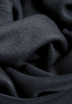 Donker marineblauwe stof, zachte textuur, iets pluizig. Het materiaal is gelaagd en gekreukt, met een geribde tailleband zichtbaar aan de onderkant.