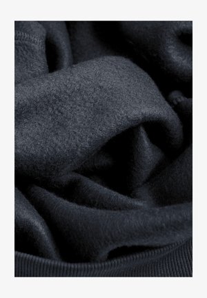 Donker marineblauwe stof, zachte textuur, iets pluizig. Het materiaal is gelaagd en gekreukt, met een geribde tailleband zichtbaar aan de onderkant.