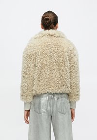 Beige Kunstpelzjacke mit lockerer Silhouette, gerippten Bündchen und strukturierter Oberfläche, kombiniert mit metallisch silbernen Hosen mit weitem Bein.