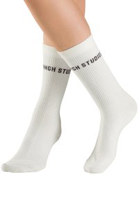 Weiße Baumwoll-Sneakersocken mit geripptem Muster. "STUGH STUDIOS" in Braun auf dem oberen Bündchen gedruckt. Symmetrisches Design mit weichem Finish.