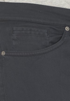 Jeans in denim blu scuro con superficie texturizzata, design a cinque tasche e accenti in metallo vicino alla vita e alle tasche.
