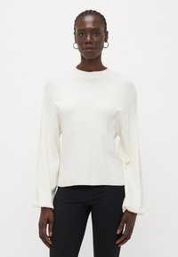Pull léger de couleur crème avec un col montant, des manches longues amples et une coupe décontractée. Texture lisse avec un motif tricoté subtil.
