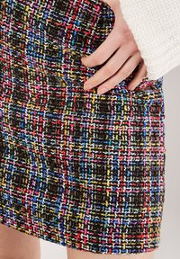 Gonna in tweed multicolore con un motivo testurizzato caratterizzato da fili neri, rossi, gialli e blu, e un dettaglio di tasca laterale.