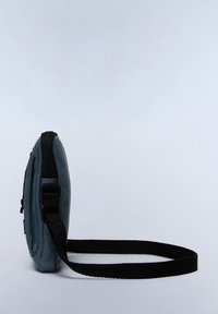 Sac à bandoulière rond en teal, avec une surface texturée, une bandoulière noire et une fermeture éclair. Design solide, taille compacte, adapté à un usage quotidien.