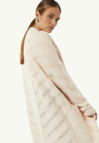 Hellrosa gestrickte Strickjacke mit offener Maschenstruktur und gestreiftem Muster. Verfügt über lange Ärmel und eine lockere Passform. Texturiertes, weiches Material mit Taschen.