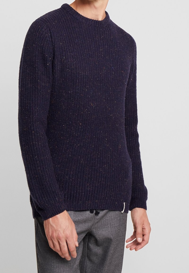 Marinblå stickad tröja med rund halsringning, ribbad textur och färgprickar genom hela tyget. Har lång ärm och rak nederkant.