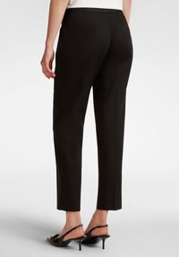 Pantaloni neri sartoriali con una vestibilità affusolata, caratterizzati da una texture liscia e una vita di media altezza, abbinati a eleganti sandaletti neri con tacco sottile.