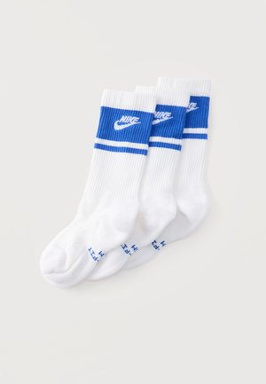 Tri biele ponožky crew s modrými pásmi a logami Nike naukladané na jednoduchom svetlom pozadí.