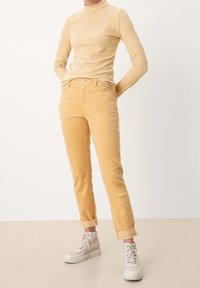 Pantaloni in corduroy giallo chiaro con taglio dritto, dotati di tasche laterali e orli arrotolati, abbinati a un top lungo a maniche con texture coordinata.
