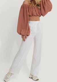 Rdzawoczerwony krótki top bez ramiączek z bufkami, zestawiony z białymi, lnianymi spodniami o wysokim stanie i beżowymi sneakersami. Gładkie tekstury w całej stylizacji.