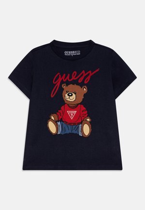 Marineblå børne t-shirt med en bjørn iført en rød sweater og jeans, og ordet "guess" i rød skrift ovenover.