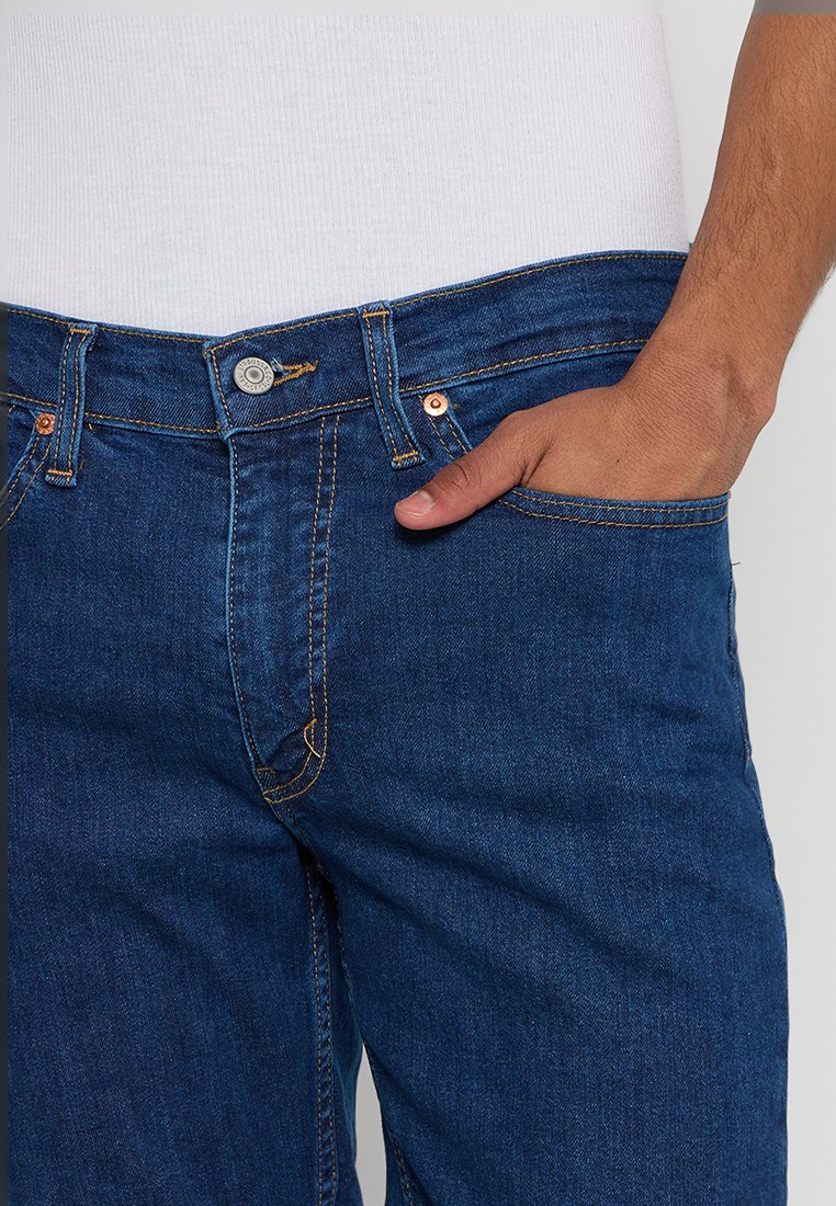 Blaue Jeans aus Denim verfügen über ein klassisches fünf Taschen Design, mit Kupfernieten und kontrastierendem gelben Nähten. Der Stoff hat eine glatte Textur.