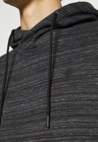 Felpa nera con texture, dotata di coulisse e logo discreto sul davanti. Il tessuto presenta un motivo melangiato e una finitura morbida.