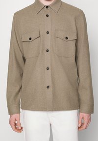 Bruin wollen overhemd met knopen en een kraag, twee borstzakken en zwarte knopen. Heeft een getextureerde, zachte afwerking en een rechte zoom.