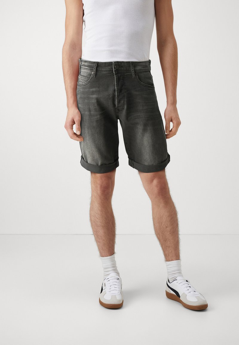 Șorturi din denim gri cu tivuri răsucite, având un design clasic cu cinci buzunare. Combinat cu pantofi sport albi și șosete albe de tip crew.