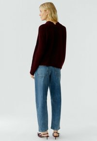 Burgundy knitted sweater with ribbed detailing, paired with light blue loose-fit jeans and dark sandals. Features a round neckline.