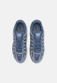 Des baskets Nike présentant un mélange de matériaux en mesh et en daim bleu clair et foncé, avec une surface texturée et des accents blancs.