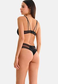 Ensemble de lingerie noire comprenant des détails en mesh transparent et en dentelle. Le bralette possède des bretelles ajustables et une fermeture par crochet, accompagné d'un string assorti.