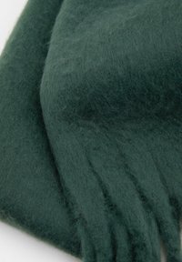 Mørkegrøn uldhalstørklæde med en blød, tekstureret overflade, der har frynsede ender og en glat fald, der fremhæver varme og komfort.