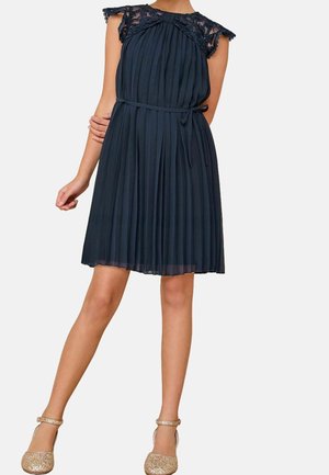 Marineblå plisseret kjole med blonde capærmer, indsnævret talje og en svævende nederdel. Accentueret med et bælte; parret med glitrende guld sko.