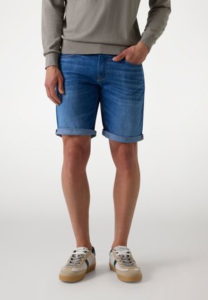 Jeans kratke hlače v svetlo modri barvi z zavihanimi robovi, s subtilnimi detajli šivanja. V kombinaciji s sivo majico in elegantnimi športnimi copati.