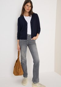 Marineblauwe cardigan met knopen, witte t-shirt, grijze jeans en beige sneakers. Bruine suede tas met een slouchy ontwerp. Glad texturen en neutrale kleuren.