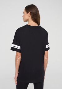 T-shirt nera con un fit rilassato, maniche corte con strisce bianche e scollatura rotonda. Il materiale sembra morbido e leggero.