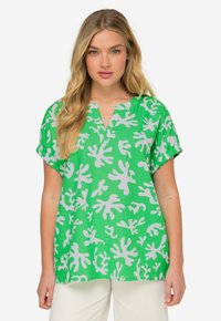 Top verde a maniche corte con scollo a V, caratterizzato da un motivo astratto bianco. Realizzato in tessuto leggero con una vestibilità comoda.