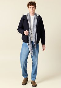 Giacca navy con fodera interna grigia, t-shirt bianca, sciarpa grigia, jeans blu e stivali marroni. L'outfit presenta una vestibilità casual e rilassata.