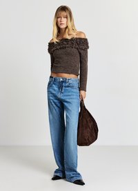 Haut marron à épaules dénudées avec des volants texturés, assorti à un jean large bleu clair et un sac en daim marron. Chaussures noires à bouts pointus.