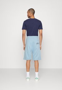 Marineblauw t-shirt met korte mouwen gecombineerd met lichtblauwe shorts met een klein bedrukt ontwerp, afgemaakt met witte sokken en schoenen met groene accenten.