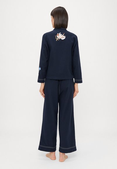 Jūras zilas mājas apģērba komplekts, kas ietver garām piedurknēm topu ar izšuvumu aizmugurē un plašām biksēm. Mīksts audums ar kontrastējošām šuvēm.