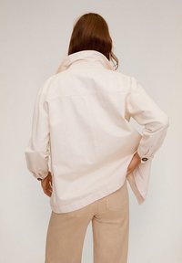 Giacca a camicia rosa chiaro realizzata in cotone, con colletto alto, vestibilità rilassata e maniche lunghe. Presenta polsini con bottoni e spacchi laterali.