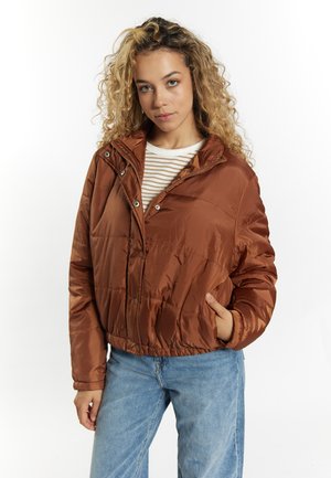 Bruine pufferjack met een capuchon, doorgestikt textuur, sluiting met drukknopen aan de voorkant en zijzakken, gecombineerd met een gestreepte lange mouw blouse en spijkerbroek.