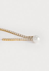 Złoty wsuwka z rzędem przezroczystych kamieni w designie w zygzak, z dużą okrągłą białą perłą na jednym końcu. Gładka tekstura i połyskujące wykończenie.