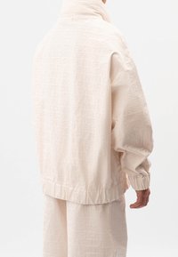 Světlé béžové zipové sako s vysokým límcem, elastickými manžetami a celoplošným vroubkovaným vzorem "FLOW". Hladká textura a volný střih.