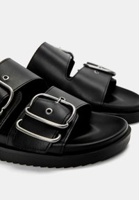 Schwarze Ledersandalen mit zwei breiten Riemen und verstellbaren silbernen Schnallen. Übergangsdesign mit einer strukturierten Gummisohle.
