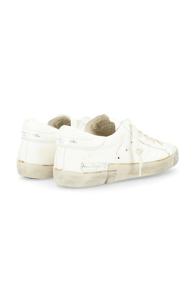 Sneakers bianchi in tela con superficie testurizzata, suole in gomma e segni di usura visibili. Presentano dettagli in marrone e cuciture, design classico.