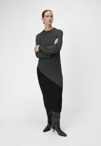 Abito lungo aderente in maglia a costine di colore grigio scuro e nero con un design asimmetrico. Presenta maniche lunghe e un collo rotondo, abbinato a stivali scuri.