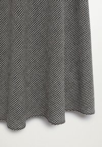Falda de patrón de espiga gris y negro con un diseño acampanado y suaves pliegues sobre un fondo blanco liso.