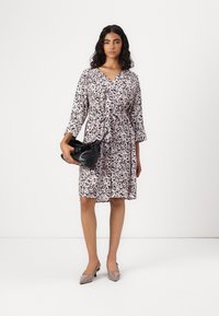 Floral print dress featuring a V-neck, tie detail at the waist, three-quarter sleeves, and a lightweight, flowing fabric. Black bag and beige heels.