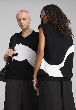 Maglione senza maniche nero in maglia con un grande design silhouette bianca, collo e orlo a coste. Il modello mostra un fit casual e uno stile rilassato.