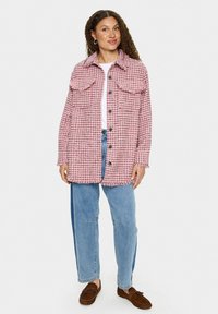 Roza in črna houndstooth jakna z dvema sprednjima žepoma, zaklepom s gumbi, frufrujem na robu in sproščenim krojem, v kombinaciji s svetlo modrimi kavbojkami.